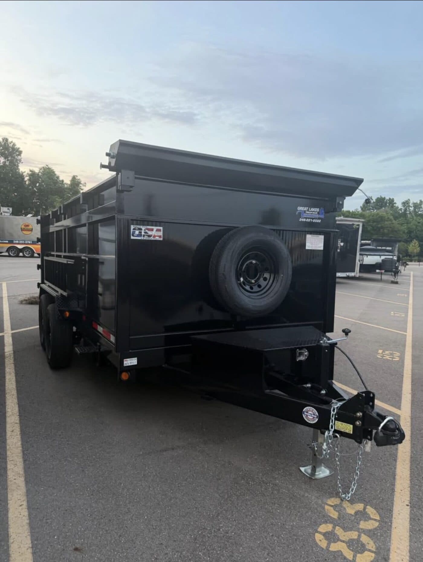 Front three-quarter view of the dump trailer showing the hitch, spare tire and toolbox